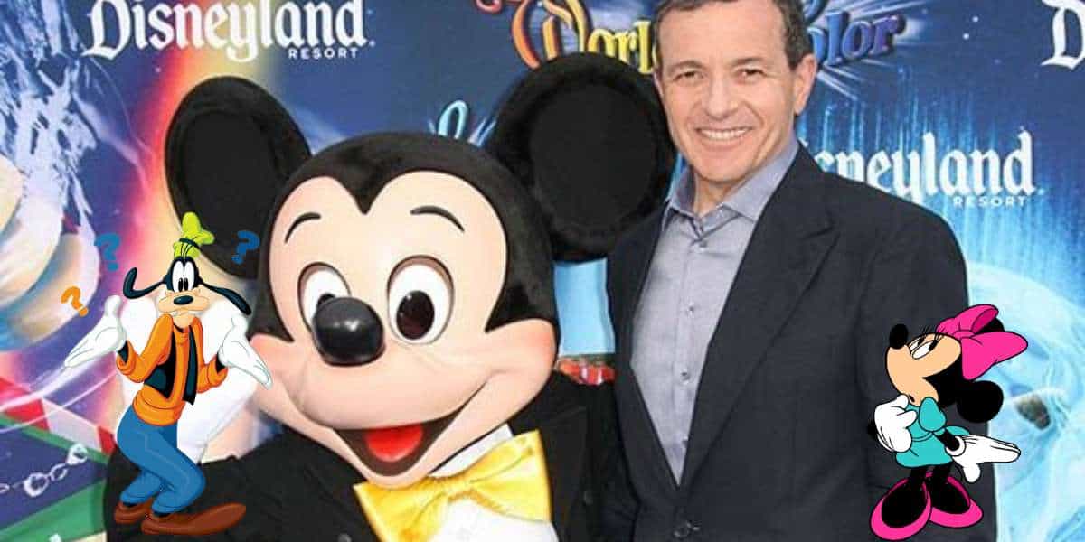 Mickey Mouse greets a guest at a Disneyland Resort event, surrounded by playful Goofy and Minnie Mouse artwork, with Disney CEO Bob Iger in attendance.