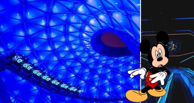 Under a stunning blue-lit geometric ceiling accented by white lights, Mickey Mouse greets guests at the entrance to TRON Lightcycle Run in Disney World, with a glimpse of the attraction’s immersive dark ride interior beyond.