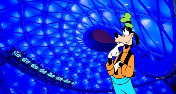 Goofy gazes up in awe beneath the glowing blue dome of the TRON Lightcycle Run Queue, clearly impressed by the cutting-edge atmosphere and futuristic details that surround him in this immersive Disney attraction.