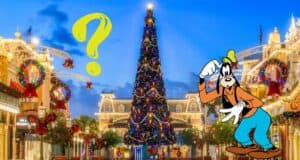 Goofy greets guests with a smile next to a big yellow question mark in a lively town square, as the towering Christmas tree glows in festive lights—reminding everyone at the Disney Parks to check their park reservations and enjoy the holiday magic.
