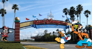 Walt Disney World entrance featuring a colorful Minnie Mouse sign, with Donald Duck and Goofy cartoon statues welcoming guests—a popular photo spot for visitors, set against the backdrop of recent headlines surrounding the "Don't Say Gay" controversy.