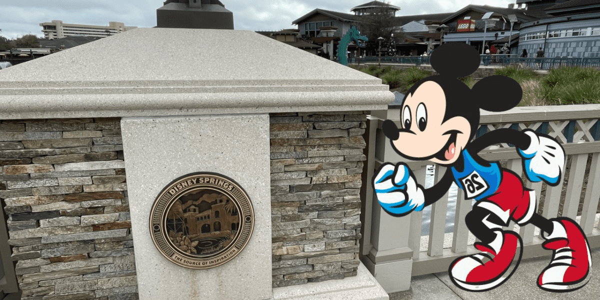 Mickey Mouse dashes past a stone post adorned with a Disney Springs plaque, embodying the excitement of runDisney festivities as lively shops and happy guests create a bustling backdrop.
