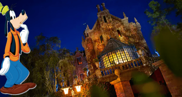 Goofy pauses thoughtfully outside the glowing, eerie Haunted Mansion at Walt Disney World, surrounded by shadowy trees that enhance the attraction’s mysterious nighttime ambiance.