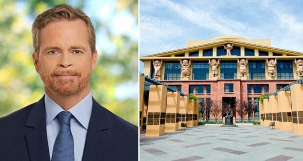 Disney CEO Mark Parker, dressed in a suit, stands next to a photo of the iconic Team Disney building, instantly recognizable by its whimsical character statues adorning the facade—a vivid tribute to the imaginative heart of The Walt Disney Company.