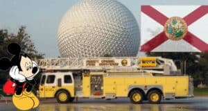Mickey Mouse poses by a bright yellow fire truck at Disney World, with the iconic Epcot geosphere and the Florida flag in the background—a scene that nods to Reedy Creek’s legacy during a time of big news around Governor DeSantis.