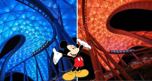 Mickey Mouse greets guests at Disney World, posing in front of dazzling blue and orange neon structures inspired by TRON Lightcycle Run’s futuristic world, all aglow under the night sky.