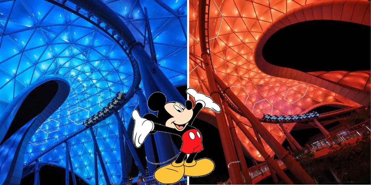 Mickey Mouse greets guests at Disney World, posing in front of dazzling blue and orange neon structures inspired by TRON Lightcycle Run’s futuristic world, all aglow under the night sky.