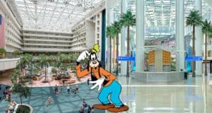 Goofy greets guests inside the spacious and vibrant Terminal C at Orlando International Airport, surrounded by tropical palm trees and travelers passing by.