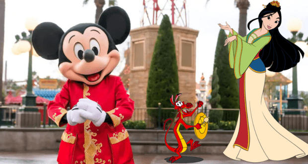 Mickey Mouse, Mushu, and Mulan pose together at Disney California Adventure, wearing vibrant Lunar New Year costumes and surrounded by festive park decor as part of the annual celebration.