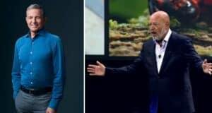 Bob Iger, smiling in a blue shirt, stands next to Bob Chapek, who gestures animatedly onstage in a black suit during a Disney Parks announcement.
