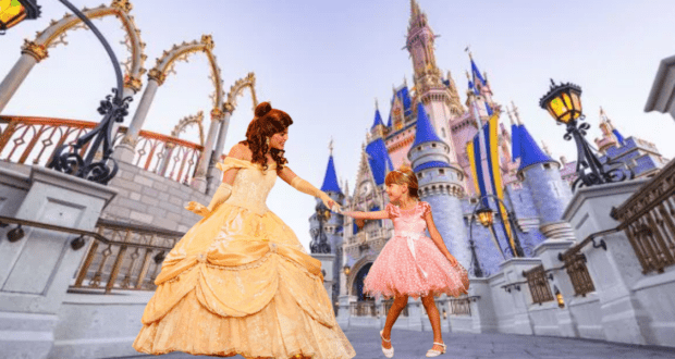 Belle in her iconic yellow ballgown greets a young guest dressed in pink outside the storybook Enchanted Tales with Belle attraction at Magic Kingdom, bringing fairy tales to life.