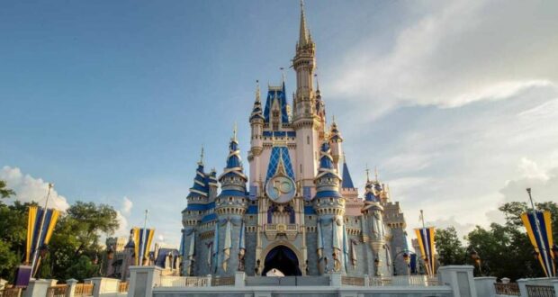 Cinderella Castle at Disney World, featuring blue and gold spires, ornate decorations, and flags, stands majestically under a clear blue sky. Inside, guests can dine like royalty at Cinderella’s Royal Table.