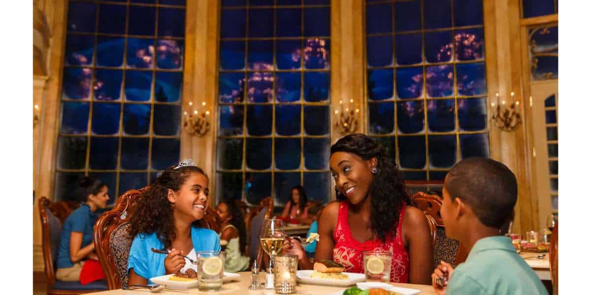 A family smiles and enjoys their Prix-Fixe dinner in a beautifully decorated Disney World restaurant, dining beneath sparkling chandeliers and soaking up the magical atmosphere.