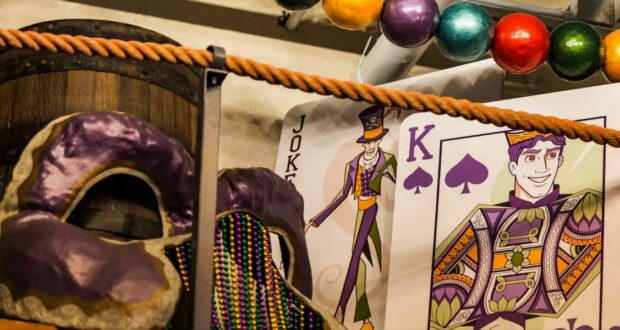 Vibrant Mardi Gras masks and shimmering beads, a Joker card, and a King of Spades card surrounded by festive decorations capture the excitement and party atmosphere that guests love at Walt Disney World Resorts.