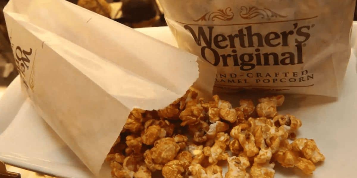 A bag and opened paper pouch of Werther's Original Hand-Crafted Caramel Popcorn delights the senses, with caramel-coated popcorn spilling onto a white tray, reminiscent of the delectable treats found among popcorn snacks at Disney World.