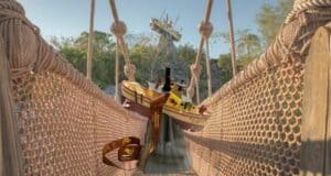 A whimsical scene at Disney’s Typhoon Lagoon features a toy boat and iconic Mickey ear hat perched on the rope bridge, with the Typhoon Tilly Sipper in view and Miss Tilly’s shipwreck atop Mount Mayday as a dramatic backdrop.