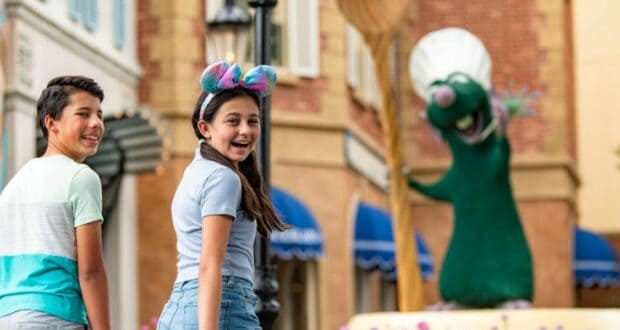 Two smiling kids stroll past the larger-than-life Remy statue from Ratatouille at EPCOT, capturing a magical Disney World photo op for Your Guide to Disney World Kingdoms.