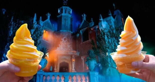 Guests enjoy cups of Halfway to Halloween DOLE Whip orange swirl soft serve in front of the Haunted Mansion at night, with the iconic spooky facade dimly lit for the festivities.