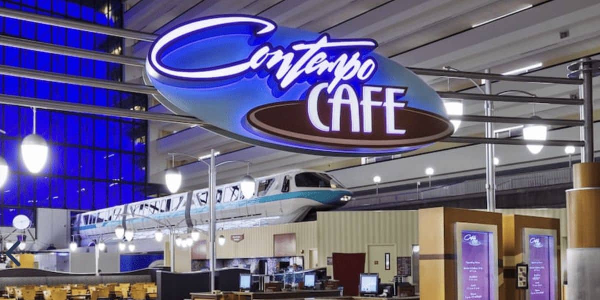 The image captures why we love dining at Disney’s Contemporary Resort: the Contempo Café sign stands proudly inside the modern building with high ceilings. In the background, a monorail glides above the café area, adorned with menu boards and hanging light fixtures.