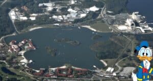 Aerial view of Epcot at Disney World, part of the sprawling 43 square miles that make up the size of Disney World, showcasing a large central lake with various buildings and attractions around it. Donald Duck, in his classic sailor outfit, is illustrated in the bottom right corner. Lush greenery and roads surround the site.