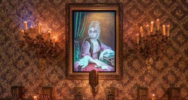 A framed portrait of a woman in 18th-century attire hangs on a wall with ornate wallpaper, reminiscent of Disney's Haunted Mansion. The woman has white hair, a pink dress, and holds a quill and book. Two antique candle sconces with lit candles flank the portrait, casting a warm glow.
