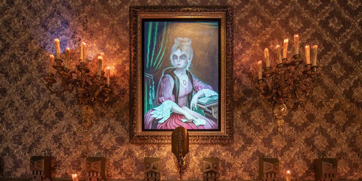 A framed portrait of a woman in 18th-century attire hangs on a wall with ornate wallpaper, reminiscent of Disney's Haunted Mansion. The woman has white hair, a pink dress, and holds a quill and book. Two antique candle sconces with lit candles flank the portrait, casting a warm glow.