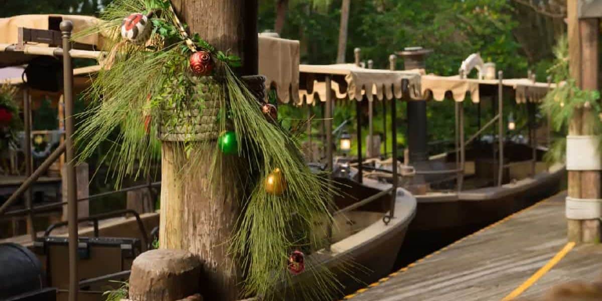 A dock with canopied boats lined up, featuring a wooden post adorned with pine branches and colorful ornaments, evokes the magic of Disney Holidays in a lush, green tropical environment.