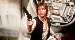 A man with brown hair, wearing a white shirt and black vest, points a blaster forward while standing in front of a large, futuristic spaceship.