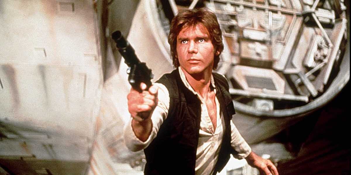 A man with brown hair, wearing a white shirt and black vest, points a blaster forward while standing in front of a large, futuristic spaceship.