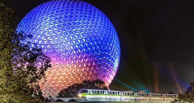 The Disney monorail glides past Epcot’s iconic, glowing Spaceship Earth at night, surrounded by lush trees in the foreground.