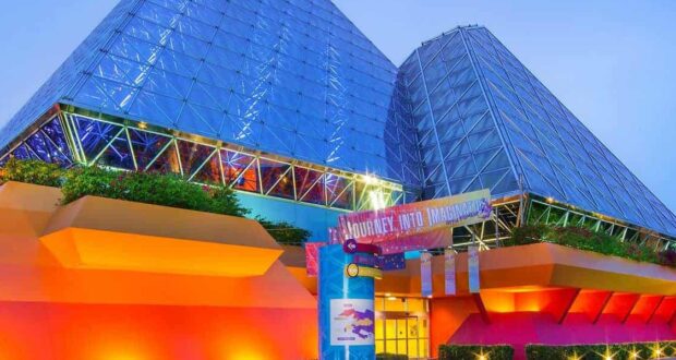 The Imagination! pavilion at EPCOT shines with colorful lights on twin glass pyramids and a welcoming "Journey Into Imagination" sign.