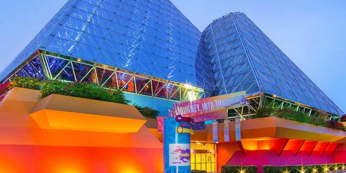 The Imagination! pavilion at EPCOT shines with colorful lights on twin glass pyramids and a welcoming "Journey Into Imagination" sign.