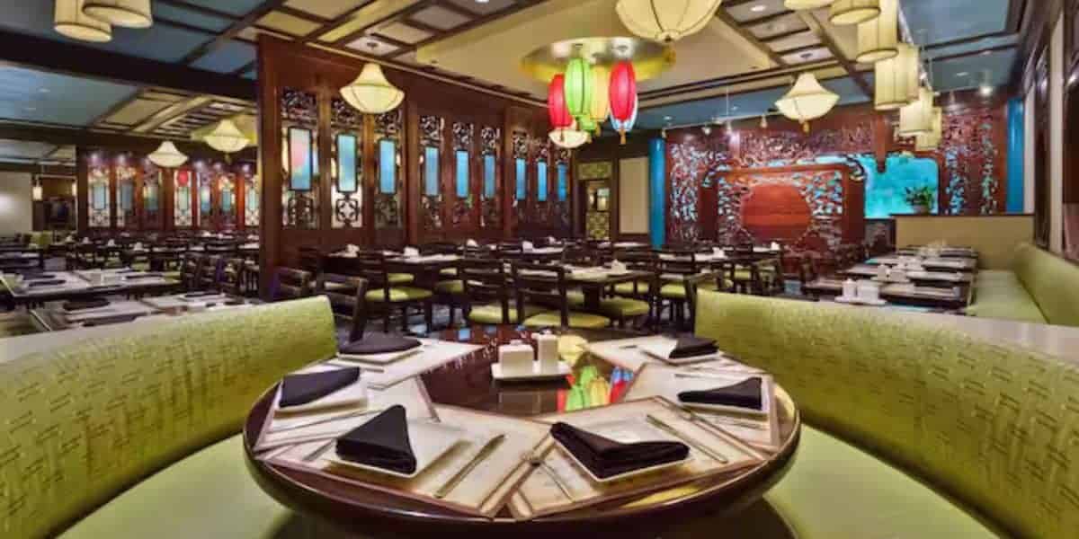 Immersive Asian-themed dining space with circular tables, vibrant green booths, glowing lanterns, and intricate wooden accents, offering guests a transporting experience reminiscent of a theme park's exotic restaurant attraction.