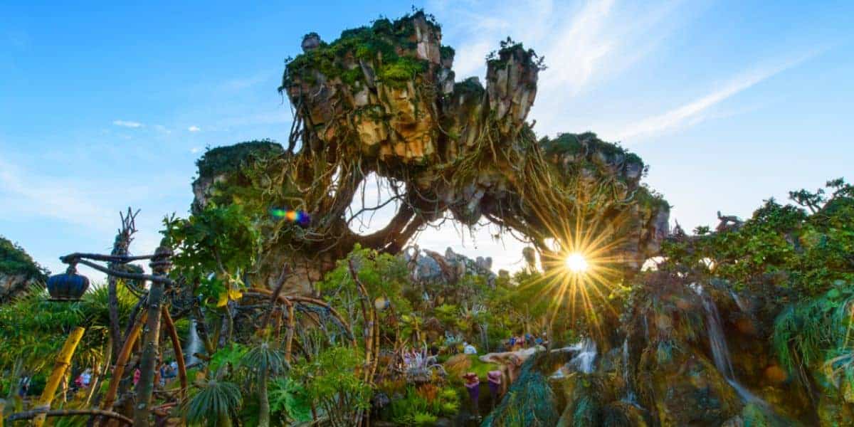 Fantasy landscape with floating mountains covered in lush greenery and vines, under a clear blue sky with sunlight streaming through. Exotic plants and pathways are visible below, creating an otherworldly atmosphere.