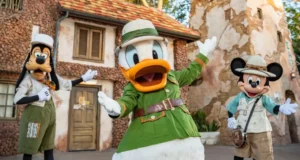 Mickey Mouse, Donald Duck, and Goofy dressed in adventurous safari gear greet guests and strike a playful pose outside a themed lodge at Disney’s Animal Kingdom.