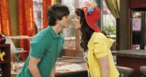 In a scene reminiscent of the vivid set designs from the Wizards of Waverly Place sequel, a young couple leans in for a kiss amid the playful atmosphere of a color-splashed, brightly lit room adorned with signature orange curtains, evoking the immersive environments familiar to fans of themed entertainment experiences.