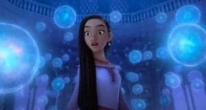 An animated heroine marvels as glowing blue orbs float around her in the magical, grand hall of a fantasy-themed attraction.