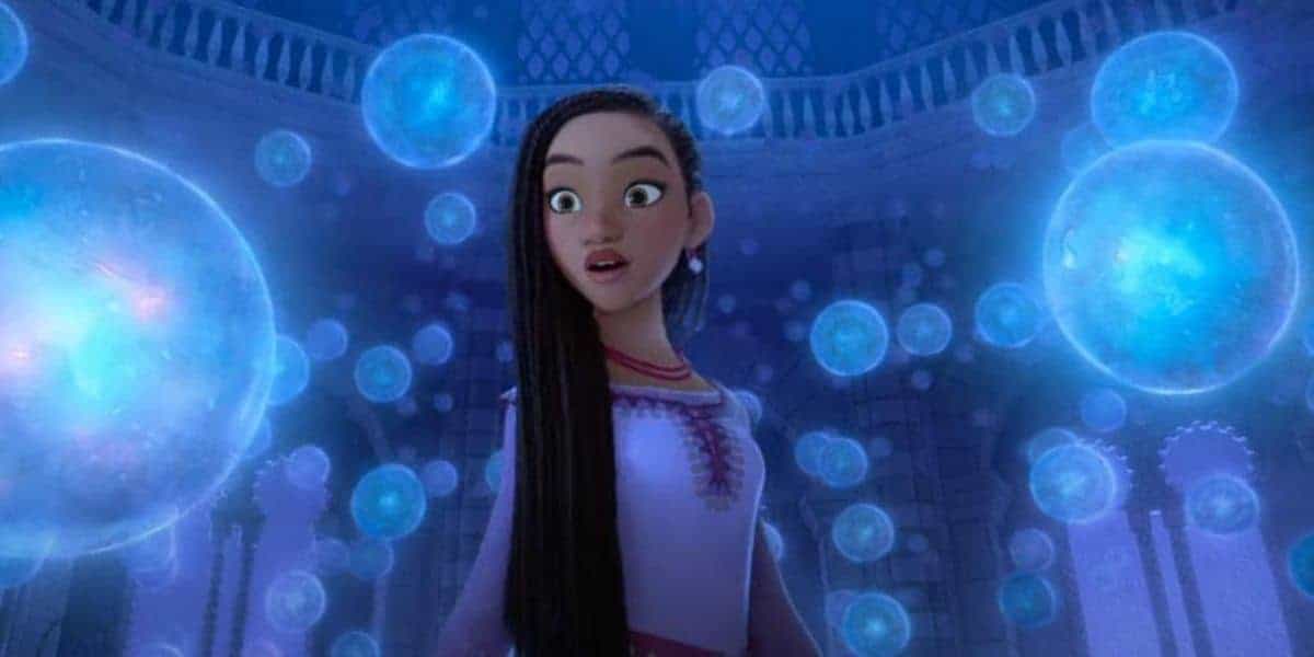 An animated heroine marvels as glowing blue orbs float around her in the magical, grand hall of a fantasy-themed attraction.