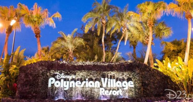 Illuminated sign of disney's polynesian village resort at night surrounded by lush palm trees and tropical plants.