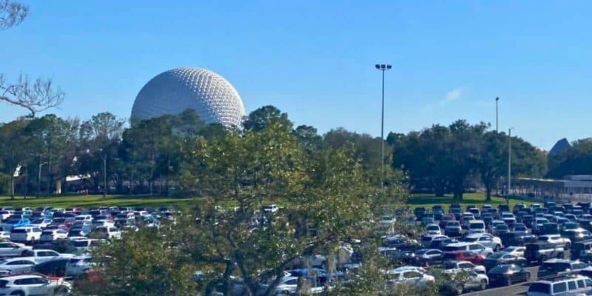 A bustling parking lot with numerous vehicles, with the iconic EPCOT geodesic sphere visible in the background against a clear blue sky.