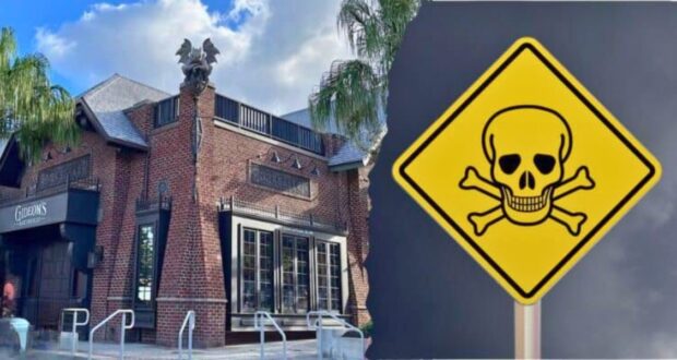 A gothic-style brick building with decorative gargoyles on the roof stands under a cloudy sky, with palm trees nearby. To the right, a yellow triangular warning sign features a skull and crossbones, evoking an eerie Disney villain scene that indicates danger or poison.