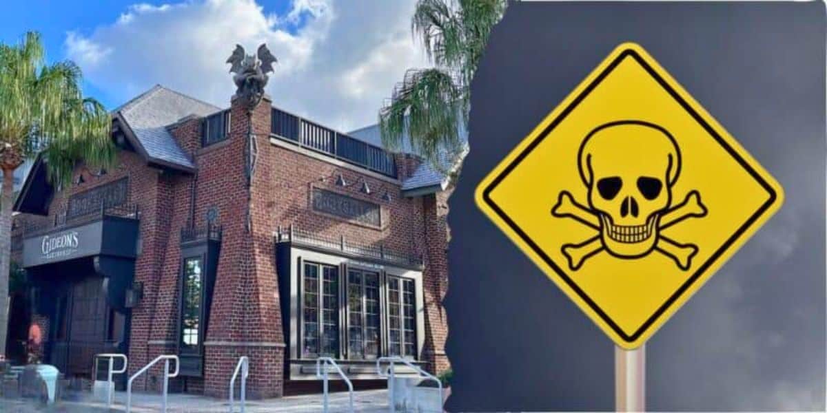 A gothic-style brick building with decorative gargoyles on the roof stands under a cloudy sky, with palm trees nearby. To the right, a yellow triangular warning sign features a skull and crossbones, evoking an eerie Disney villain scene that indicates danger or poison.