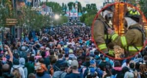 A crowded amusement park, reminiscent of Disneyland, bustling with numerous visitors wearing casual clothing and headgear. Inset within a red circle is an image of two firefighters in uniform and helmets from the Fire Department, standing close to each other with one gently touching the other's chest.
