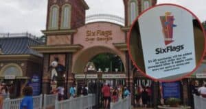 Entrance of Six Flags Over Georgia theme park with a sign in the foreground noting a $1.30 surcharge for orders due to increased labor and supply costs. People are visible near the gates.