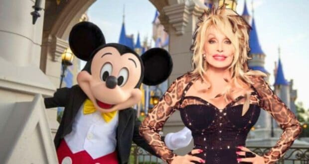 In front of a castle backdrop, a person dressed as Mickey Mouse stands next to a woman with blonde hair wearing a black dress with leopard print sleeves. Both are smiling and posing for the camera.
