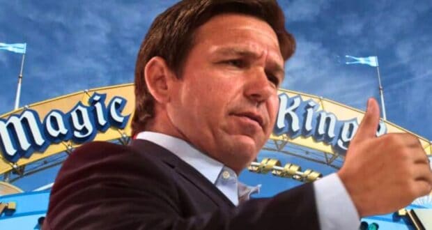 Ron DeSantis giving a thumbs up in front of the Magic Kingdom entrance sign under a blue sky.
