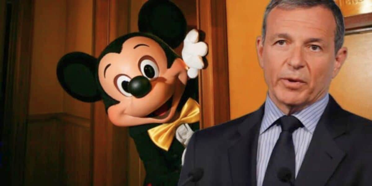A person in a Mickey Mouse Disney costume peeking out from behind a wooden door, next to a man in a suit giving a speech.
