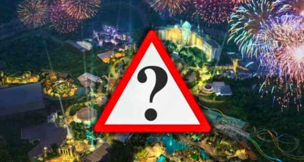 An aerial view of the Epic Universe theme park at night shows it illuminated with various lights and vibrant fireworks in the sky. The park appears bustling with attractions, rides, and green areas. A large warning sign with a question mark is superimposed in the center.