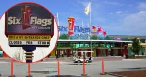 The entrance to Six Flags New Orleans shows a sign stating "Closed for Storm". The park entrance is empty with the main entrance gate and flags visible in the background, set against a blue sky. Orange safety barriers and a small vehicle are also visible.