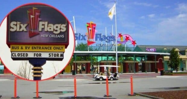 The entrance to Six Flags New Orleans shows a sign stating "Closed for Storm". The park entrance is empty with the main entrance gate and flags visible in the background, set against a blue sky. Orange safety barriers and a small vehicle are also visible.